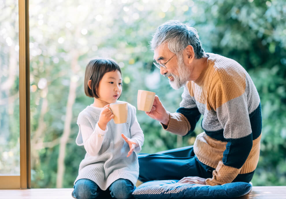 親子とマグカップ: 陽当たりの良い縁側で、孫と祖父が笑顔で飲み物を飲む様子。